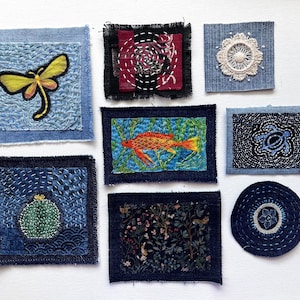 May include: A collection of eight fabric patches featuring various embroidered designs including a yellow dragonfly, a red fish, a green cactus, a blue turtle, a white lace medallion, a floral pattern, and geometric stitching on denim and dark fabric.