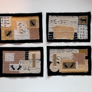 May include: Four rectangular fabric collages featuring black cat silhouettes, beige and brown textured patches, and Japanese calligraphy. Each piece is framed by a black border and incorporates various patterns including dots, geometric shapes, and frayed edges.
