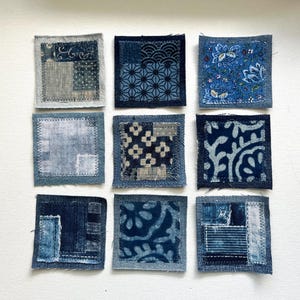May include: Nine small, square fabric patches in shades of blue, arranged in a grid. Each patch features a unique pattern, including floral, geometric, and abstract designs. The patches are hand-stitched with visible seams, showcasing a handcrafted aesthetic.