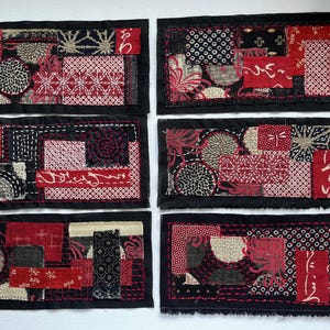 May include: Six rectangular fabric patches with a black border. Each patch features a patchwork design in shades of red, black, and cream, with various patterns including floral and geometric motifs. The patches are likely handmade.