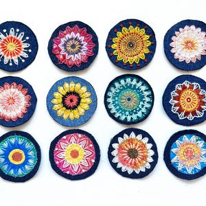 May include: Twelve circular fabric patches featuring intricate, multi-colored floral embroidery on a dark blue denim background. Each patch displays a unique radial pattern with varied thread colors including yellow, red, pink, white, and teal.