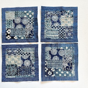 May include: Four square fabric patches with a denim border. Each patch features a unique design of indigo blue and white stitched patterns, including floral and geometric motifs. The patches are arranged on a white surface.