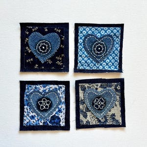 May include: Four square fabric patches with denim borders. Each patch features a denim heart with a floral applique. The backgrounds of the hearts vary, including dragonfly and floral patterns in shades of blue and white. The patches are arranged on a white surface.