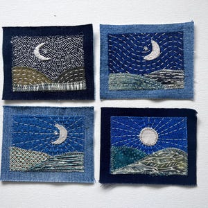 May include: Four rectangular denim fabric patches featuring hand-stitched embroidery of night landscapes. Each patch displays a moon or sun above rolling hills, rendered in various shades of blue, green, and white thread on denim backgrounds.