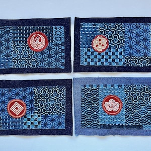 May include: Four rectangular patches with a dark blue denim border. Each patch features a unique combination of blue patterned fabrics and a red circular emblem with white detailing. The patches are likely for decorative or craft purposes.