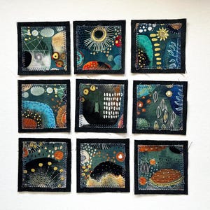 May include: Nine square fabric patches arranged in a grid, each featuring abstract designs in shades of teal, navy, orange, and white. The patches have dark fabric borders with visible zigzag stitching along the edges of the colorful patterns.