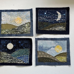 May include: Four small fabric art pieces depicting landscapes. Each square has a dark blue denim border. The scenes include a sun, moon, stars, and rolling hills in shades of green, blue, and yellow. The art is created with fabric and embroidery.