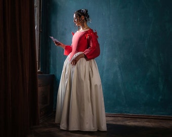 May include: A woman in a red and white dress stands in a room with a teal green wall. She is holding a piece of paper in her hand and looking down at it.