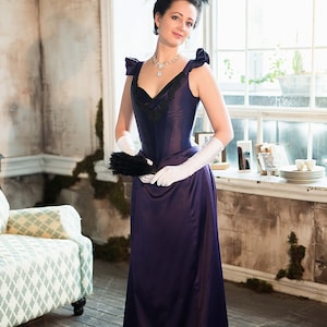 May include: A woman in a long, dark purple dress with a black lace bodice and a white feather hat. She is holding a black fan and wearing white gloves.