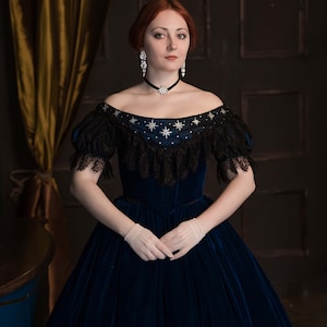 May include: A woman wearing a dark blue velvet gown with a black lace overlay and a star-shaped embellishment. She is wearing white gloves and a silver necklace with a star pendant.