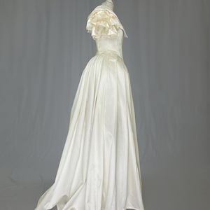 May include: A white satin wedding dress with a ruffled neckline and a full skirt.