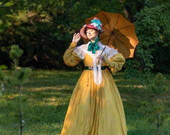 May include: A woman in a yellow dress and a red and green hat holds a brown parasol in a grassy park.