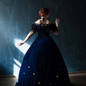May include: A woman wearing a dark blue velvet gown with a low neckline and a star-shaped pattern. The gown has a full skirt and is worn with white gloves.