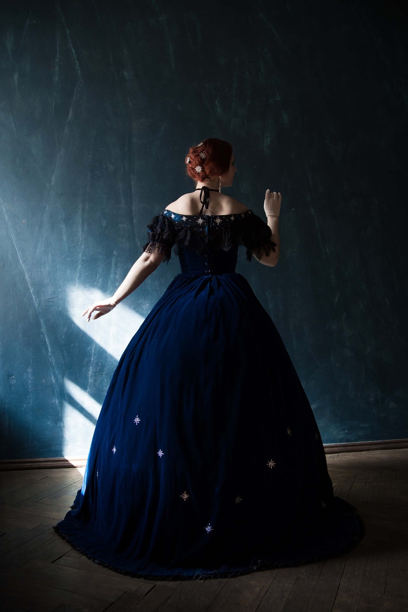 May include: A woman wearing a dark blue velvet gown with a low neckline and a star-shaped pattern. The gown has a full skirt and is worn with white gloves.
