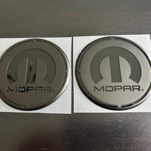May include: Two black round stickers with the Mopar logo and the word "Mopar" in white lettering.