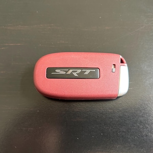 May include: A red car key fob with the word "SRT" printed in black on the front.