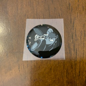May include: A black and white cartoon character with a black hat and sunglasses. The character is wearing a black suit and is holding a microphone. The image is on a black background.