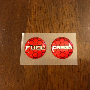 May include: Two round red and black stickers with a honeycomb pattern. The stickers say "FUEL" and "CARGO" in white letters.