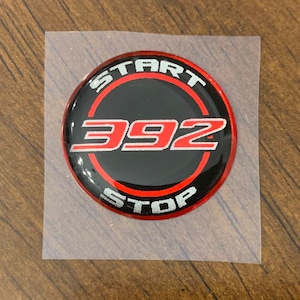May include: A round, black and red sticker with the words "START" and "STOP" in a circle around the number "392" in silver and red.