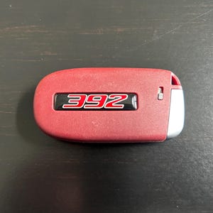 May include: A red car key fob with a black and red number "392" on the front.