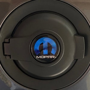 May include: A black fuel door with a blue and silver Mopar logo.
