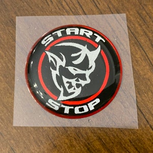 May include: A black and red round sticker with a white silhouette of a demon head inside a red circle. The text "START" and "STOP" are written in a white, stylized font around the circle.