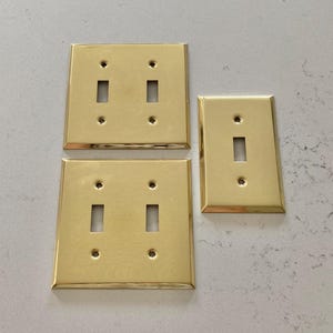 Three vintage brass switch plates; two 2-gang switch plates and one 1-gang switch plate