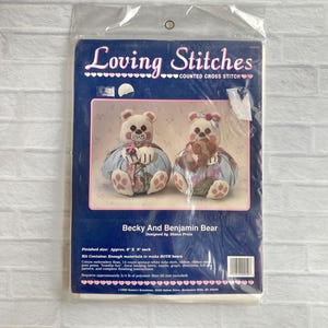 May include: A sealed package for a counted cross stitch kit. The package features a blue background with the text "Loving Stitches" and an image of two teddy bears. The kit is for "Becky and Benjamin Bear" and is designed by Diana Prain.