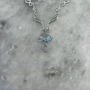 Puede incluir: Collar de plata con un delicado dise&ntilde;o de alas y un colgante de cristal azul. El colgante presenta un peque&ntilde;o amuleto de estrella.