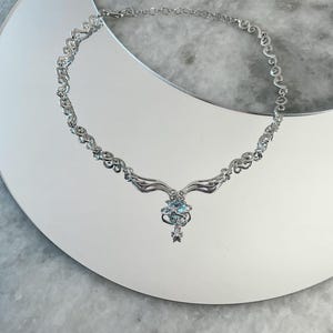 Puede incluir: Un collar de plata con un dise&ntilde;o delicado e intrincado. El colgante presenta un grupo de piedras preciosas azules y una estrella.