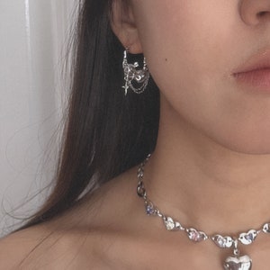 Puede incluir: Un collar de plata con un colgante de coraz&oacute;n y una cadena de plata con peque&ntilde;os corazones y piedras de colores. El collar lo lleva una persona con el pelo largo y oscuro y pendientes de plata con un dise&ntilde;o floral.