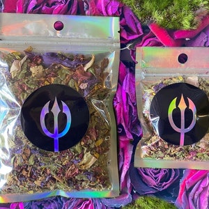 May include: Two clear, resealable bags filled with dried herbs and flowers. Each bag has a black circular sticker with a trident design. The bags are on a background of pink roses and green moss.