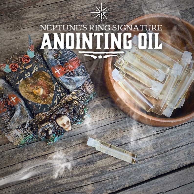 Op de afbeelding: Anointing olie flesjes en een decoratief, sierlijk object met een schedel- en hartontwerp worden getoond op een rustiek houten oppervlak. De tekst "NEPTUNE'S RING SIGNATURE ANOINTING OIL" is zichtbaar. Een houten kom bevat extra flesjes.