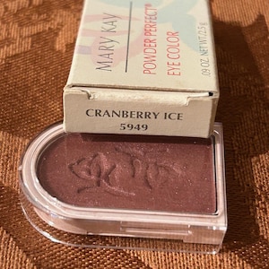 May include: A Mary Kay Powder Perfect Eye Color compact in Cranberry Ice, shade 5949. The eyeshadow is a deep reddish-brown color with a subtle shimmer. The packaging includes a cardboard box with the brand name and product details.