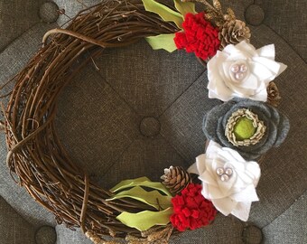 May include: A brown twig wreath decorated with white felt flowers, red felt flowers, green felt leaves, gold glitter sprigs, and pine cones.
