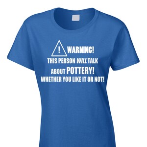 May include: A royal blue t-shirt with white text and a warning symbol. The text reads: "WARNING! THIS PERSON WILL TALK ABOUT POTTERY! WHETHER YOU LIKE IT OR NOT!" A humorous pottery-themed tee.