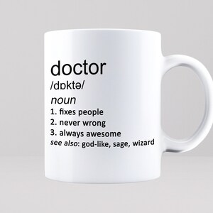 May include: White ceramic mug with a black design that defines the word "doctor" as a noun. The definition includes the phrases "fixes people", "never wrong", and "always awesome".