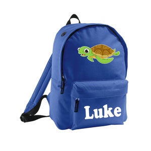 Könnte beinhalten: Ein königsblauer Rucksack mit einem Cartoon-Schildkröten-Design und dem Namen "Luke" in Weiß. Der Rucksack hat eine Vordertasche, schwarze Träger und einen oberen Griff. Die Schildkröte hat einen grünen Körper und einen braunen Panzer.