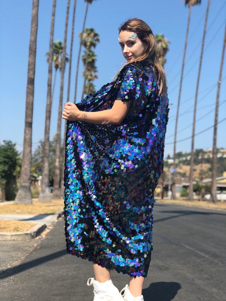 Puede incluir: Un kimono largo, azul y negro iridiscente con lentejuelas, de manga corta. El kimono est&aacute; hecho de peque&ntilde;as lentejuelas superpuestas que crean un efecto brillante.
