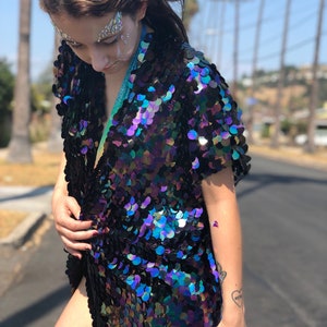 Puede incluir: Un kimono negro con lentejuelas iridiscentes de abertura frontal larga. Las lentejuelas est&aacute;n dispuestas en forma de escamas y tienen un brillo iridiscente azul, verde y morado.