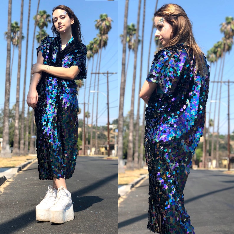 Puede incluir: Una mujer lleva un vestido de lentejuelas negro y azul iridiscente con mangas cortas. El vestido tiene un corte holgado y llega hasta la rodilla. La mujer lleva zapatos de plataforma blancos.