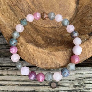 May include: A bracelet made with pink, gray, and brown gemstone beads. The bracelet is on a wooden surface.