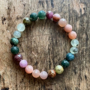 May include: A multi-colored gemstone bracelet with round beads in shades of green, pink, and brown. The bracelet is made of natural stones and is strung on elastic.