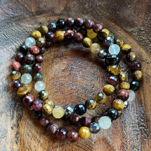 May include: A multi-strand bracelet made of tiger's eye, red jasper, and hematite beads. The bracelet has a mix of gold, brown, red, and black beads.