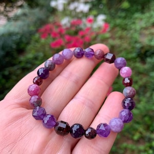 May include: A purple, pink, and green gemstone bracelet with faceted beads. The bracelet is made of amethyst, rose quartz, and green aventurine.