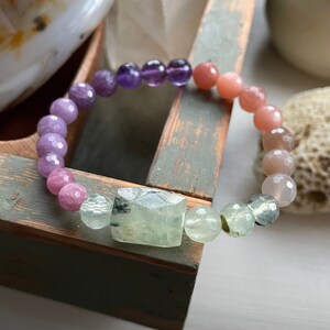 May include: A multi-colored gemstone bracelet with purple, pink, and green beads. The bracelet is made with natural stones and has a unique, layered look.