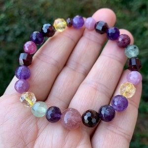 May include: A multi-colored gemstone bracelet with beads of amethyst, garnet, citrine, rose quartz, and green aventurine.