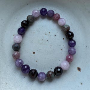 May include: A purple, pink, and black beaded bracelet with a variety of gemstone beads.