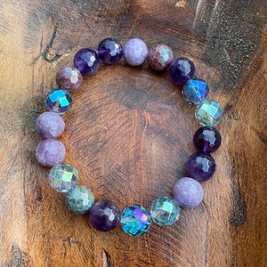 May include: A purple, blue, and green gemstone bracelet with iridescent beads. The bracelet is made with amethyst, lepidolite, and crystal beads.
