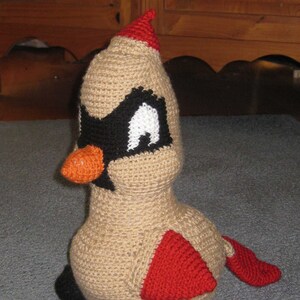 May include: A crocheted cardinal bird plush toy with a red crest, black eyes, and an orange beak. The toy is beige with a red wing and tail.